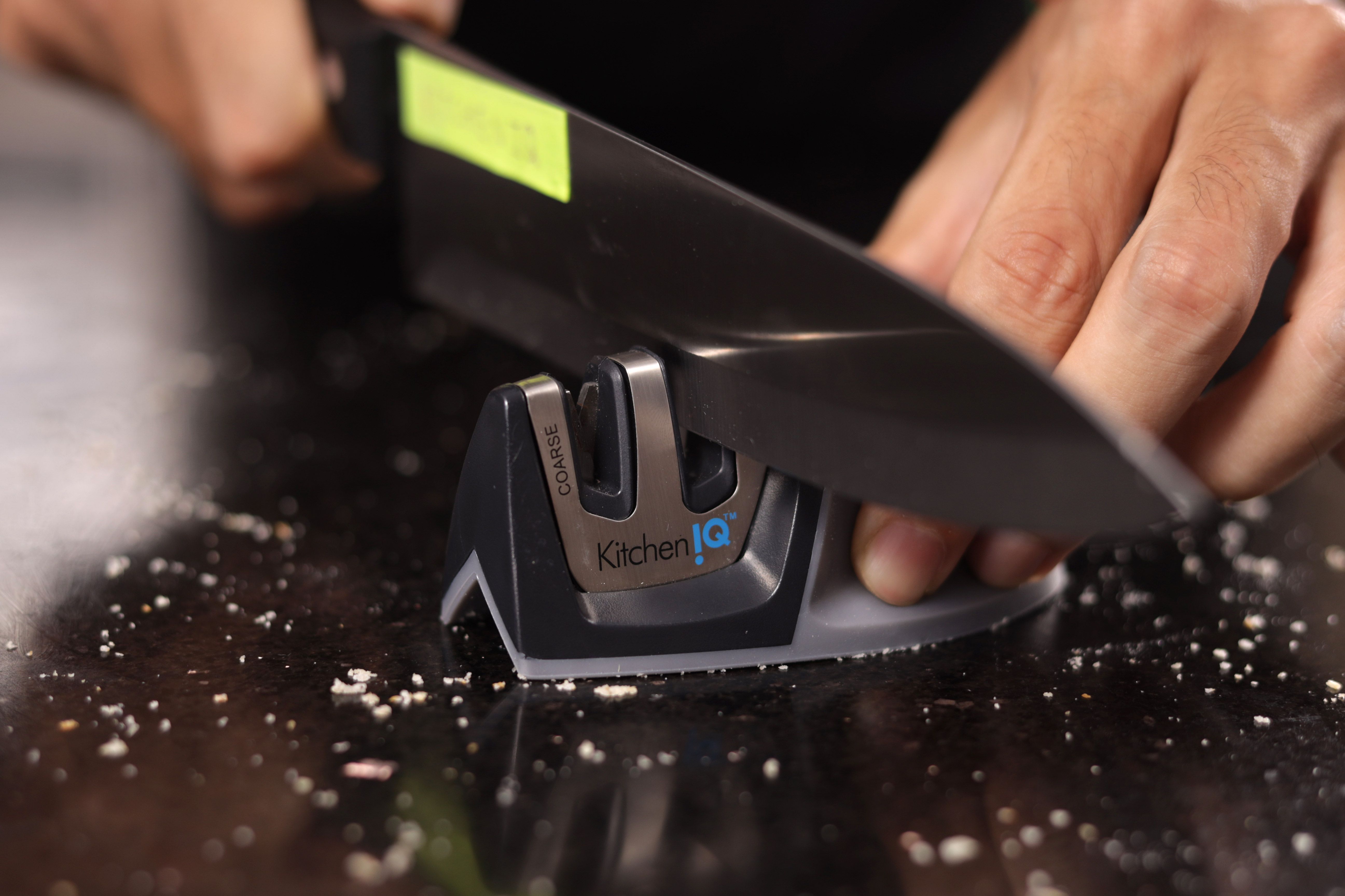 Two hands holding and sharpening a knife with the KitchenIQ on a salt-sprinkled countertop