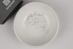 A bowl containing metal sharpening residue next to the base of the Amesser A-65 manual knife sharpener