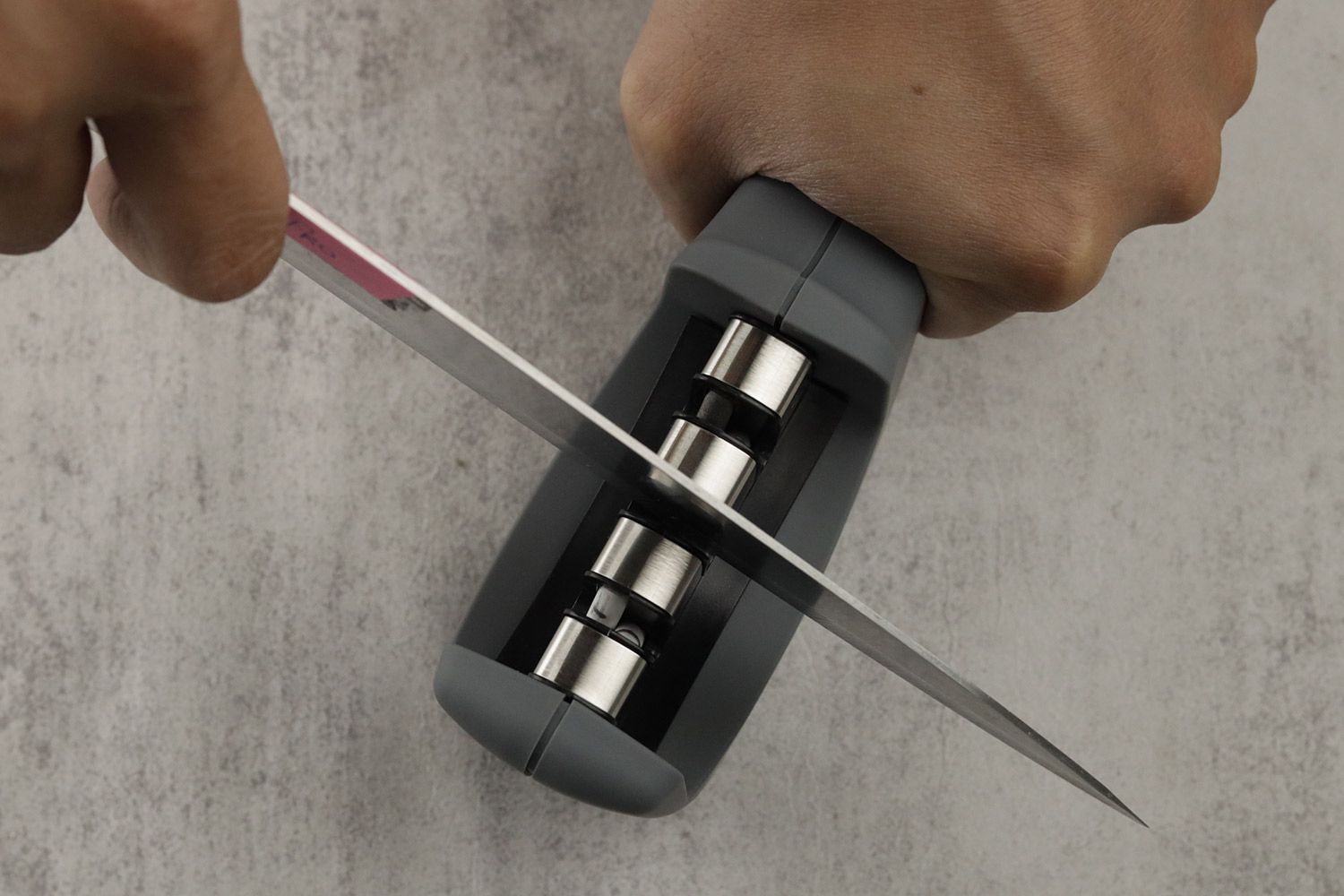 Top view of a knife being sharpened with the Amesser 3-slot knife sharpener, with the user’s two hands visible