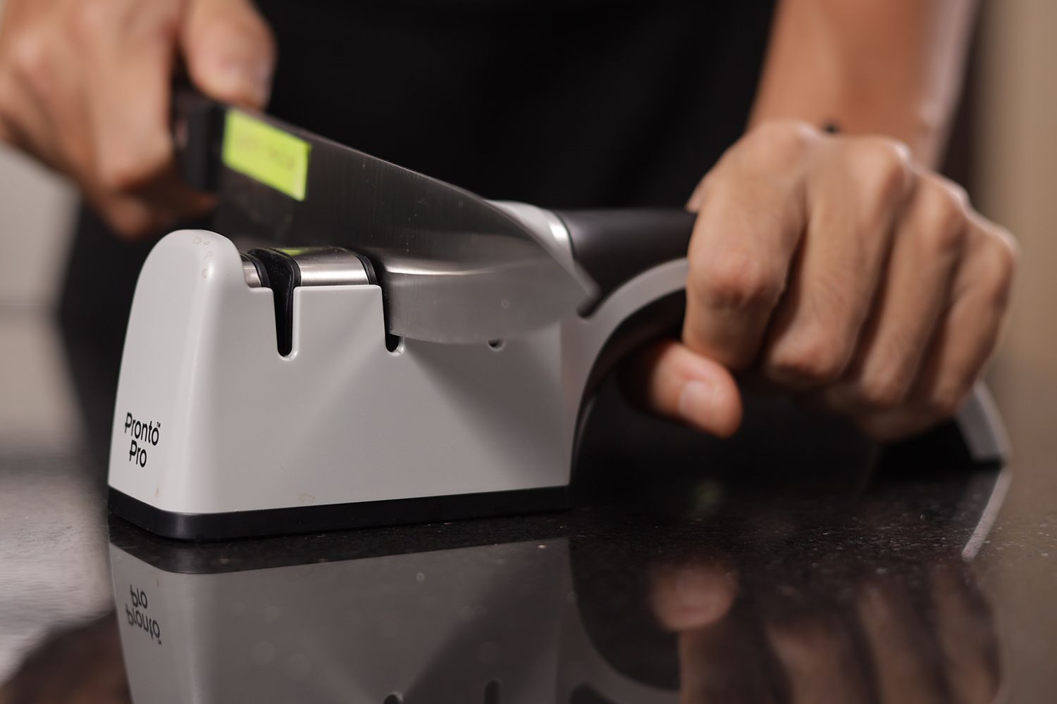 2 hands holding and sharpening a kitchen knife with the Chef's Choice sharpener