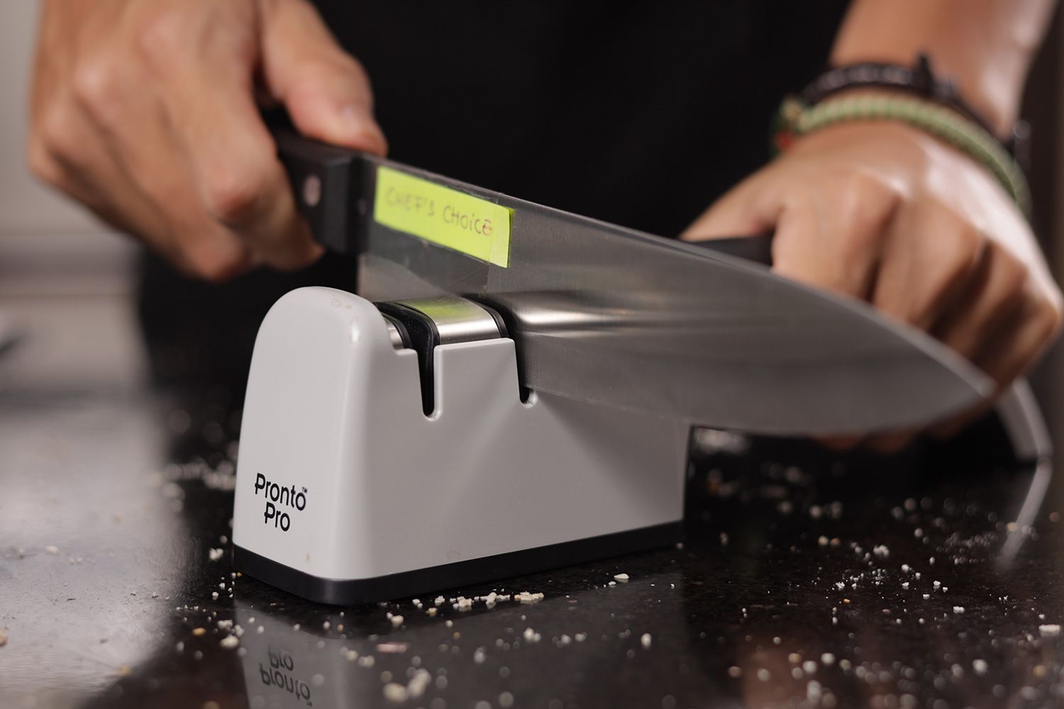 2 hands holding and sharpening a kitchen knife with the Chef's Choice on a salt-sprinkled countertop