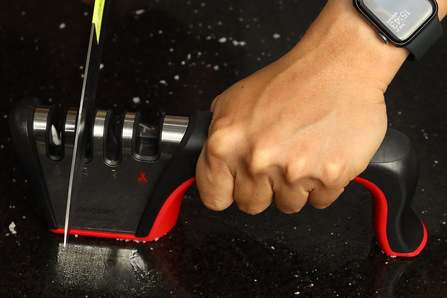 A kitchen knife being sharpened with the Longzon on a countertop with salt particles