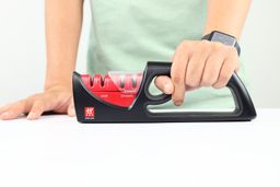 A hand holding the Zwilling knife sharpener and a hand resting on the table