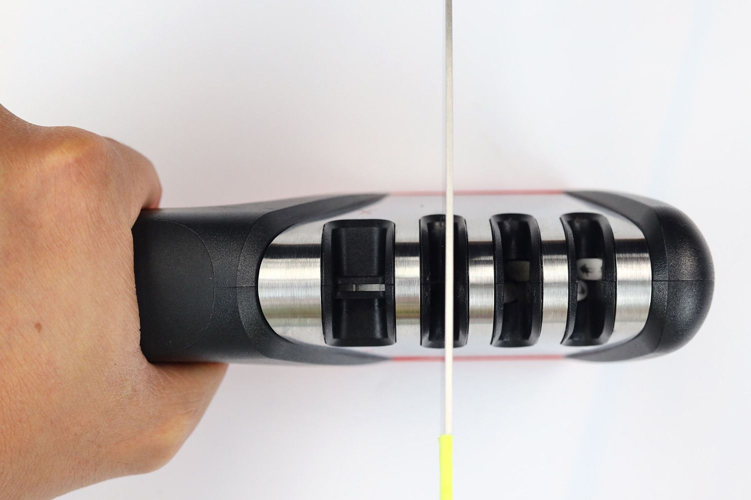 Top view of a kitchen knife in one of the Mueller’s abrasive slots, the sharpener being held by one hand