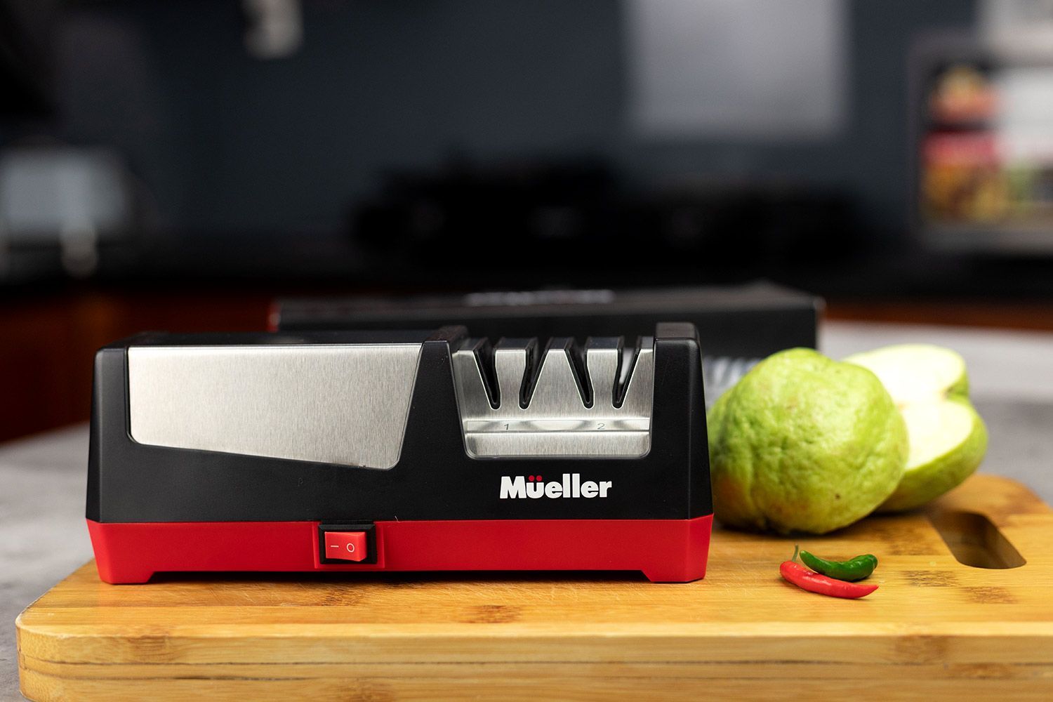 The Mueller Ultra-edge Electric Knife Sharpener on cutting board, chili peppers, guava.