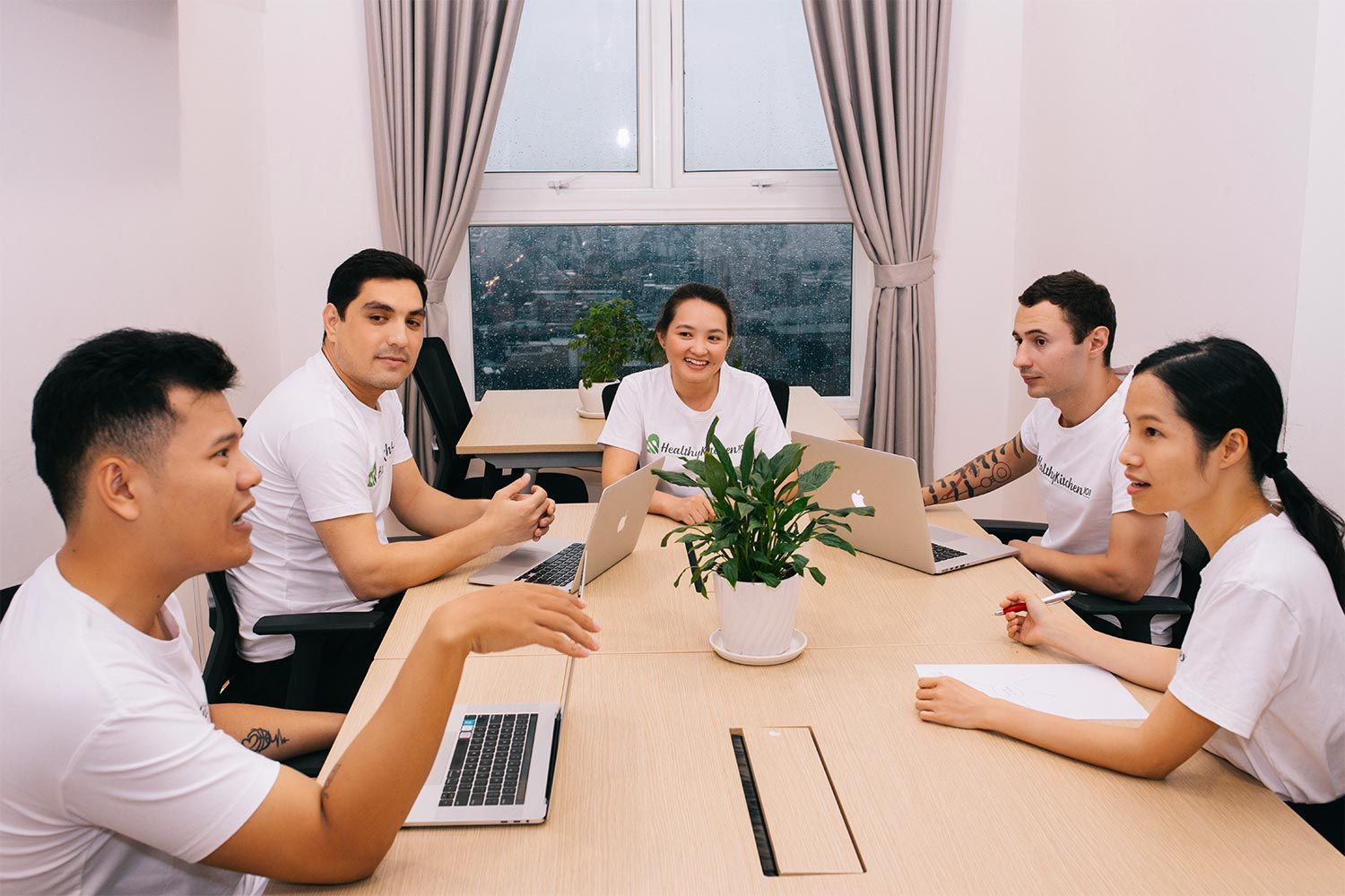  People discussing at a table, with laptop computers and plant on the table