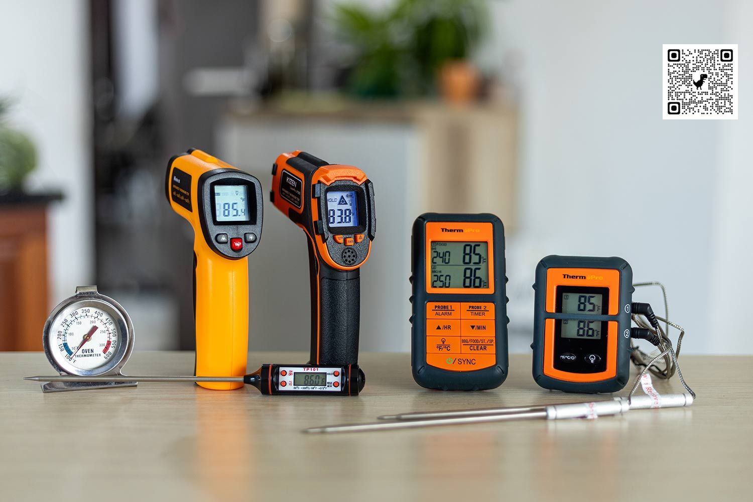 The best thermometers (oven, infrared, and meat thermometers) arranged in a line on a table against a blurred background.