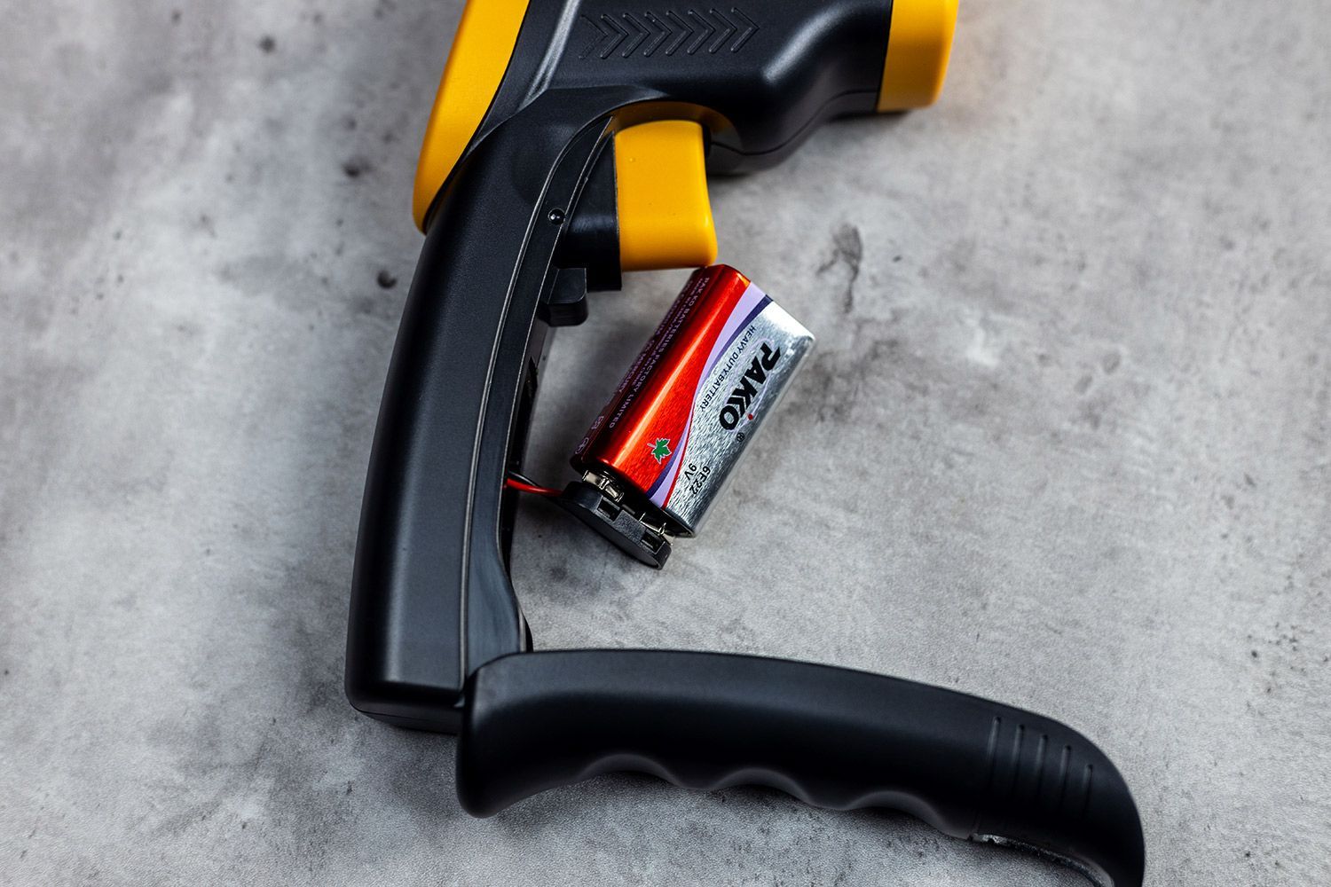 The door of the battery compartment is opened on the Etekcity Lasergrip 800 IR thermometer, revealing the 9V battery cell inside and connecting wires.