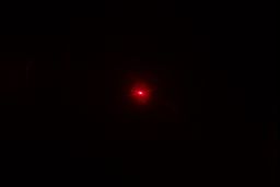 The red laser dot of the Helect IR thermometer gun’s laser emitter in a dark room.