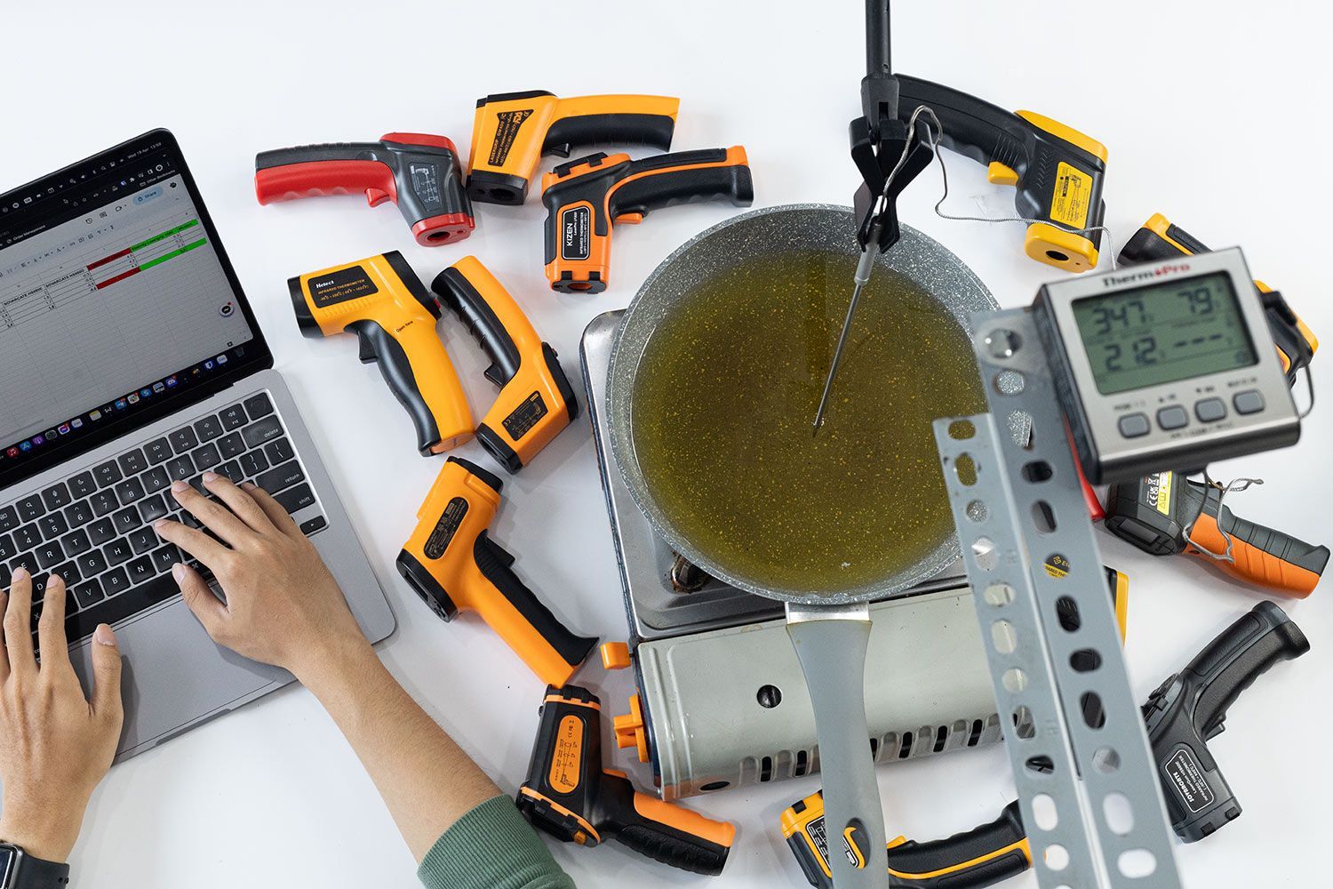 A stovetop is heating up a pan full of cooking oil with a temperature probe dipped into the oil.