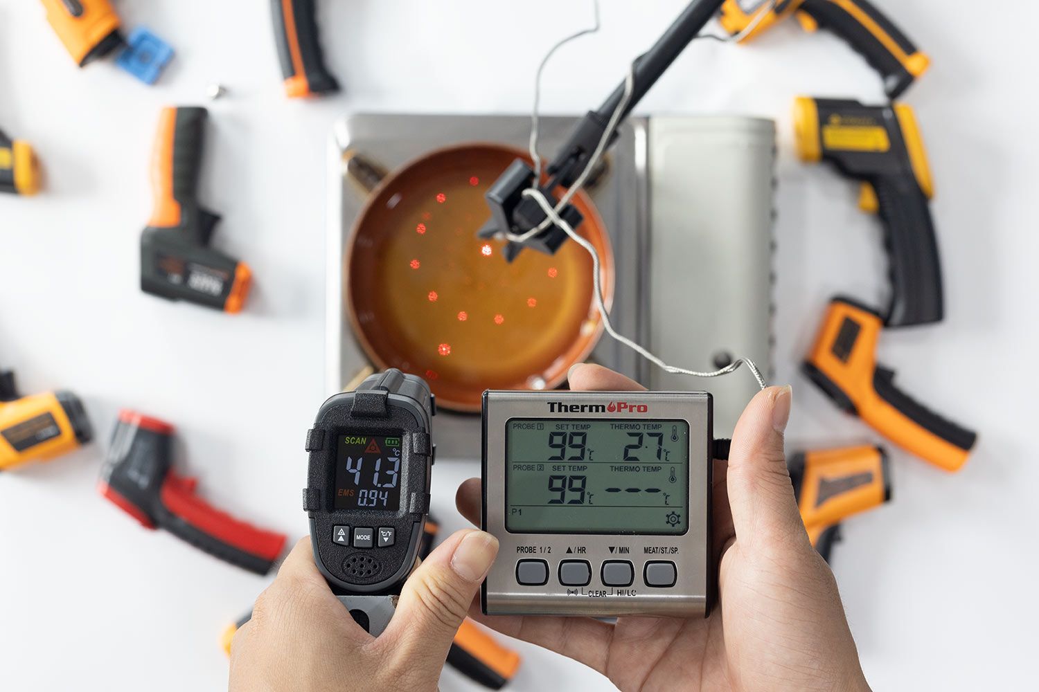 A reviewer is holding a black IR thermometer to measure the temperature of boiling oil in a pan. The screen reads 42.5°C.