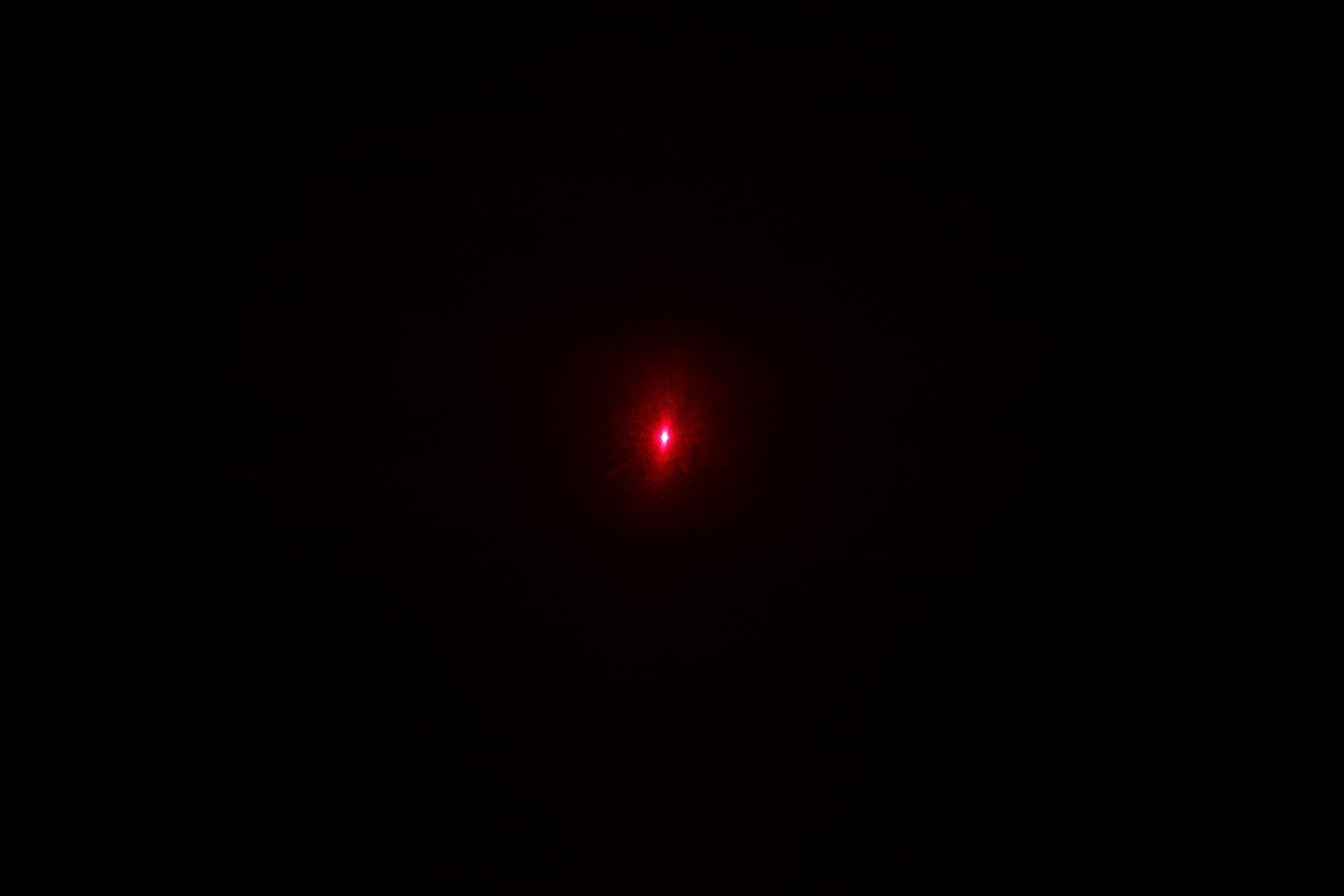 The red single-dot laser from the laser emitter of the Kizen LaserPro LP300 on the wall of a dark room.