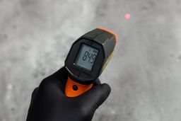 The black-gloved hand of a reviewer holding and using the Klein Tools IR1 IR thermometer in scan mode. A red laser dot can be seen in the background.