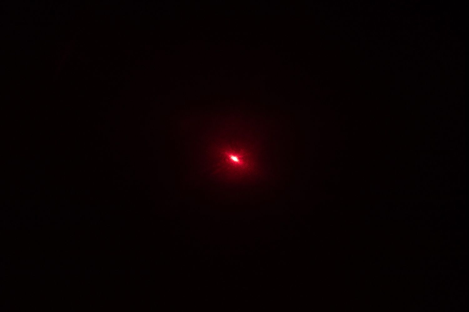 The red laser dot of the Smart Sensor AS530 IR thermometer’s laser emitter in a dark room.