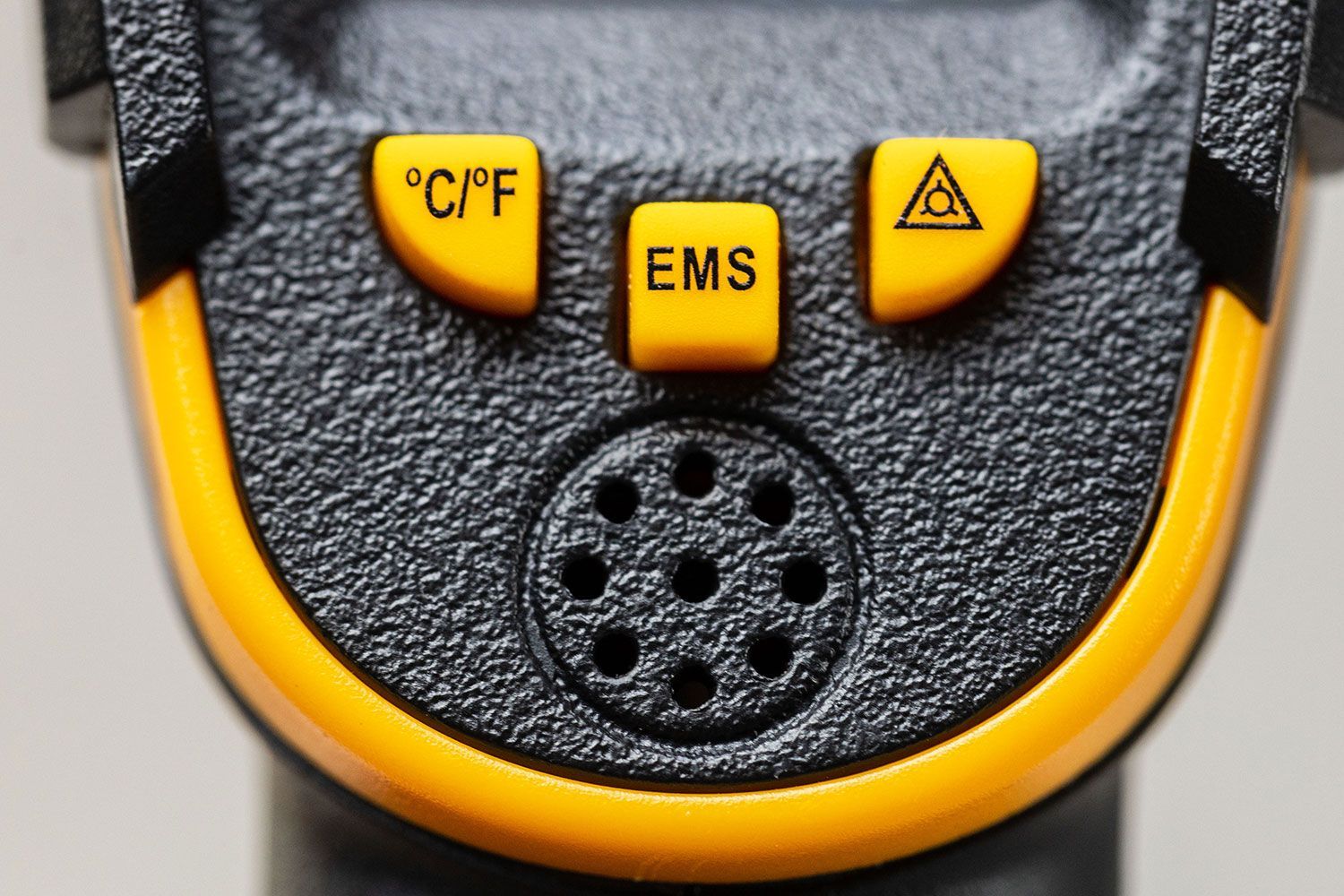 The control panel and the speaker holes on the Sovarcate HS960D IR thermometer. The button reads “°C/°F”, “EMS”, and symbol for the laser light.