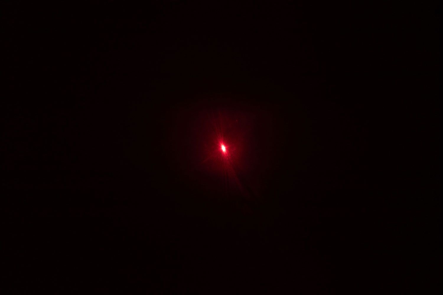 The bright red single-dot laser beam of the Sovarcate HS960D IR thermometer in a dark room.