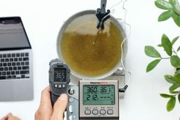 The Sovarcate HS980E IR thermometer measuring the temperature of cooking oil from 12 inches. The screen reads 36.5°F.