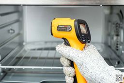 The ThermoPro TP-30 IR thermometer in the white-gloved hand of a reviewer, who’s using it to measure the internal temperature of a toaster oven.