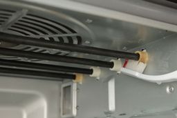 A hand brushing the stained upper heating elements’ ends inside the cooking chamber of the Cuisinart TOA-60 Convection Toaster Oven Air Fryer with baking soda and water.