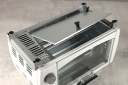 On a grey background, the bottom of the Comfee CFO-BB101 Toaster Oven has a detachable crumb tray, four stands, and holes.