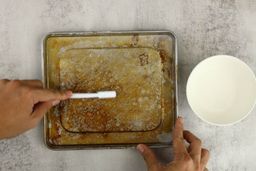 Brushing the stained silver baking pan of the Hamilton Beach 31401 4-Slice Toaster Oven with a bowl of baking soda and water.