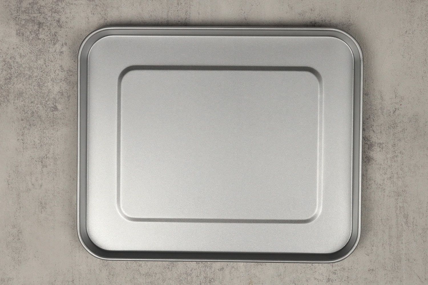 A silver baking pan of the stainless steel Hamilton Beach 31127D 6-Slice Easy Reach Toaster Oven on a grey background.