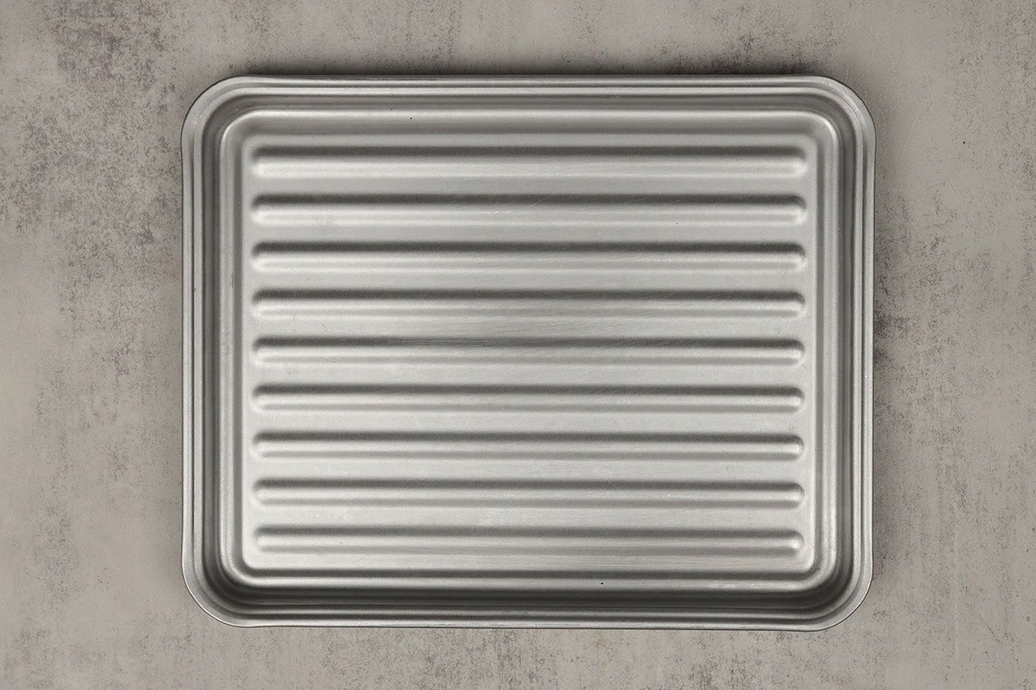 A grooved silver baking pan of the Toshiba AC25CEW-BS Convection Toaster Oven on a grey background.