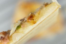 The cross-section of a toaster oven baked pizza slice showing the crust. In the background is a pizza inside a baking tray.