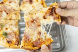 Two hands break apart a slice of pizza with melty cheese, meat, and green bell peppers on top baked using a toaster oven.