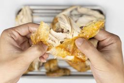 Two hands holding a piece of chicken breast roasted in a toaster oven. The skin is golden brown and the meat is cooked.