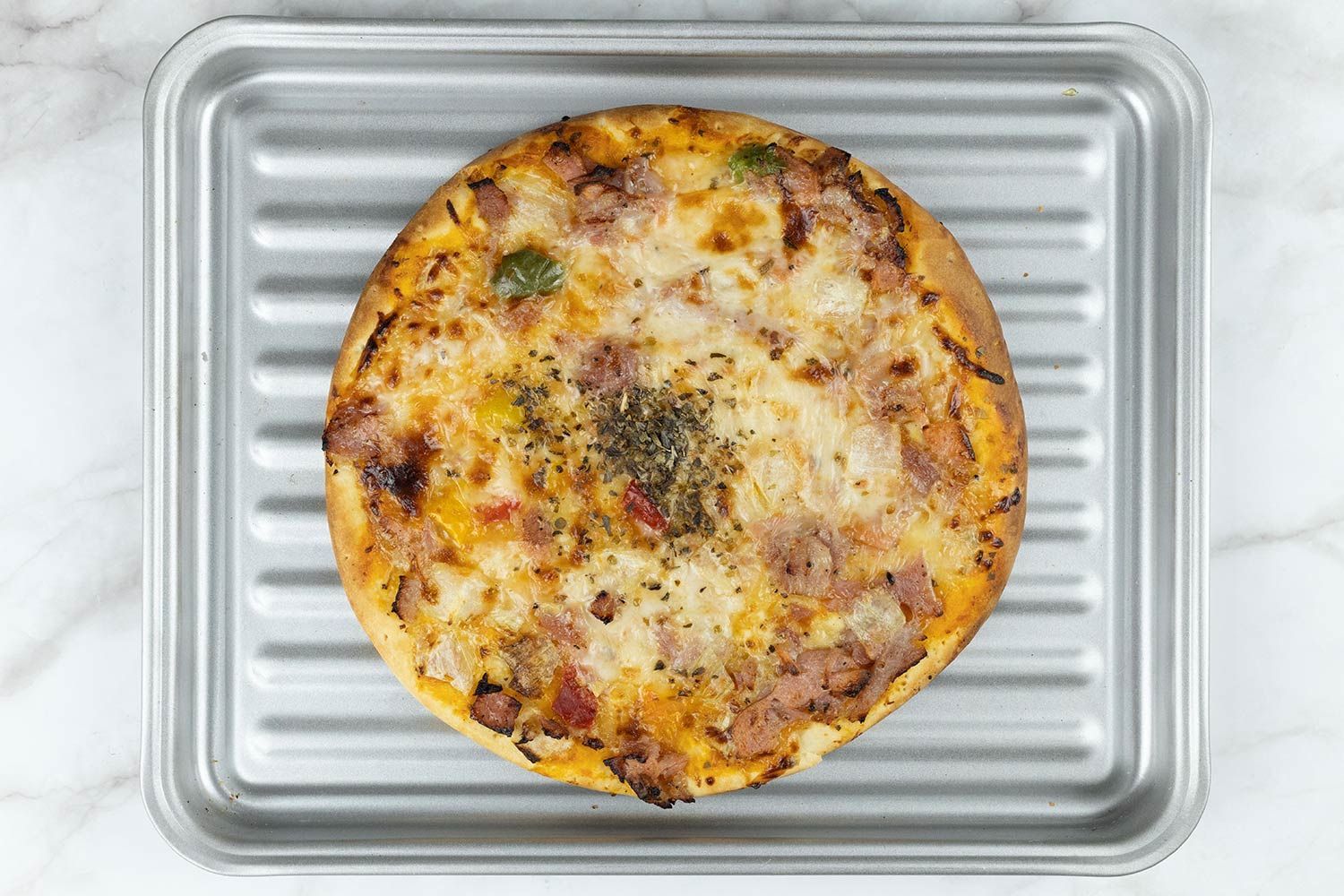 A toaster oven baked 9-inch thick-crust meat pizza with cheese, onions, and green bell peppers on top inside a baking pan.