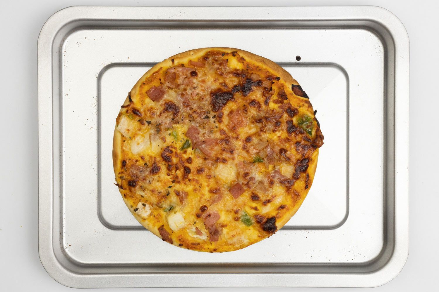 A toaster oven baked 9-inch thick-crust meat pizza with cheese, onions, and green bell peppers on top inside a baking pan.