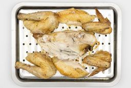 Seven pieces of a carved chicken including a carcass, two breasts, two wings, and two thighs on a silver baking pan.