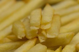 Six pieces of broken-up baked french fries are stacked on top of pieces of whole fries on a silver baking pan.