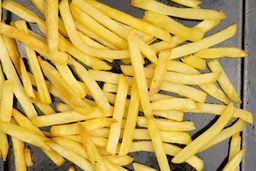 A close-up of pieces of baked french fries using a toaster oven on an enamel baking pan on a white background.