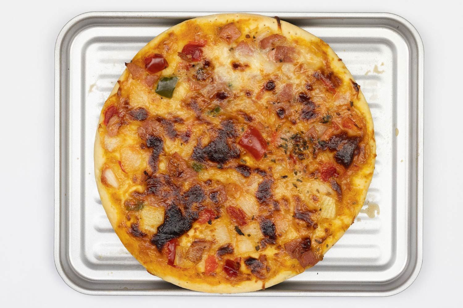 A toaster oven baked 9-inch thick-crust meat pizza with cheese, onions, and green bell peppers on top inside a baking pan.