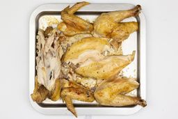 Seven pieces of a carved chicken including a carcass, two breasts, two wings, and two thighs on a silver baking pan.