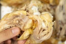 Two hands pulling apart a roasted chicken thigh. In the white background is the rest of the roasted chicken on a baking pan.