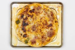 A toaster oven baked 9-inch thick-crust meat pizza with cheese, onions, and green bell peppers on top inside a baking pan.