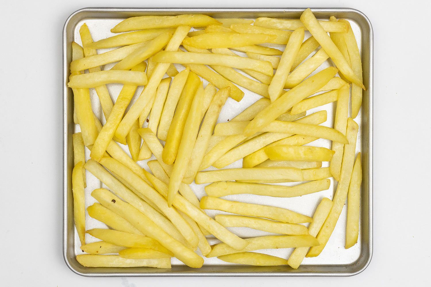 Pieces of baked french fries using the Hamilton Beach 31401 Toaster Oven on a silver baking pan on a white background.