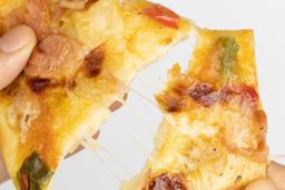 Two hands break apart a slice of pizza with melty cheese, meat, and green bell peppers on top baked using a toaster oven.