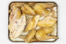 Seven pieces of a carved chicken including a carcass, two breasts, two wings, and two thighs on a silver baking pan.