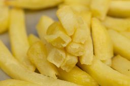 Eight pieces of broken-up baked french fries are stacked on top of pieces of whole fries on a silver baking pan.