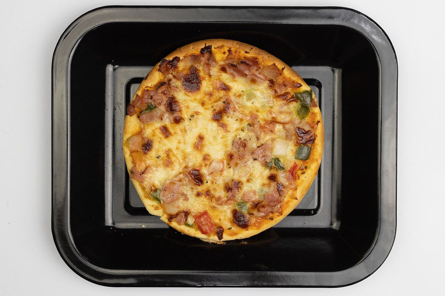 A toaster oven baked 9-inch thick-crust meat pizza with cheese, onions, and green bell peppers on top inside a baking pan.