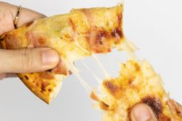 Two hands break apart a slice of pizza with melty cheese, meat, and green bell peppers on top baked using a toaster oven.