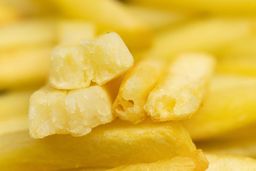 Six pieces of broken-up baked french fries are stacked on top of pieces of whole fries on an enamel baking pan.