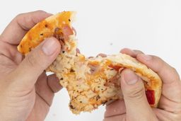 Two hands break apart a slice of pizza with cheese, meat, onions, and green bell peppers on top baked using a toaster oven.