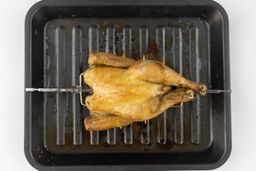 A whole roasted rotisserie chicken using the Cosori CO130-AO Oven belly up on a grey baking pan on a white background.