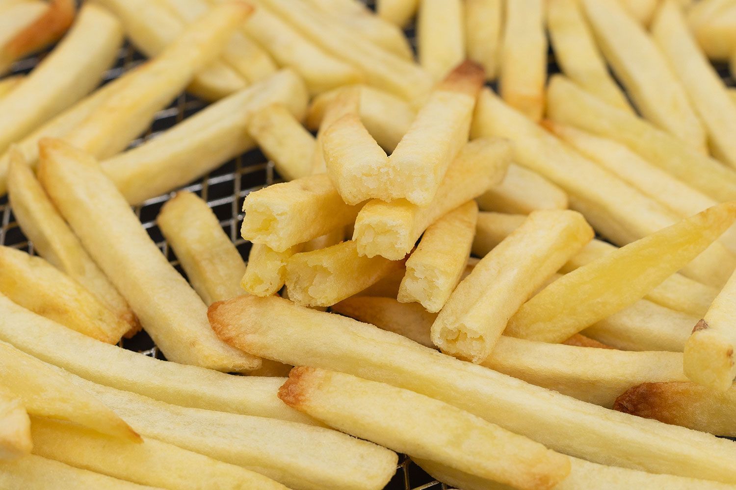 Eight pieces of broken-up baked french fries are stacked on top of pieces of whole fries inside an air fryer basket.