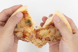 Two hands break apart a slice of pizza with cheese, meat, onions, and green bell peppers on top baked using a toaster oven.